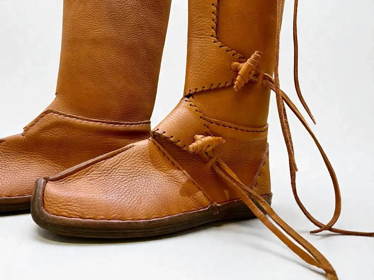 Handmade tan medieval leather boots with wrap laces, visible stitching, and full-grain texture for LARP or SCA reenactment.